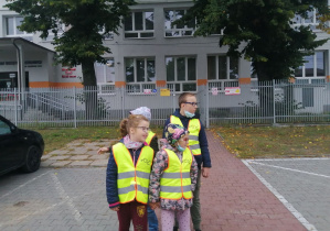 Uczniowie stojący przed szkołą przy krawędzi ulicy.
